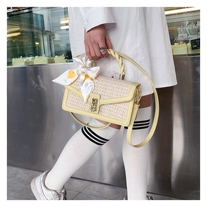 Detail of woven straw handbag with yellow leather trim, metal lock and patterned silk scarf