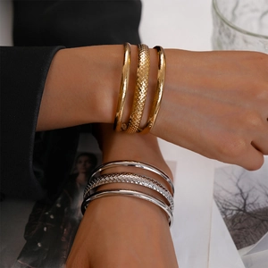 Detail of layered gold and silver textured metal bangles worn on a model wrist