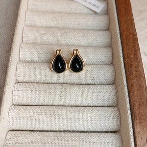 Detail shot of teardrop-shaped gold and black stud earrings on a beige linen jewelry display