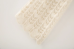Detailed macro view of cream knit sweater featuring scalloped edges and hollow crochet patterns