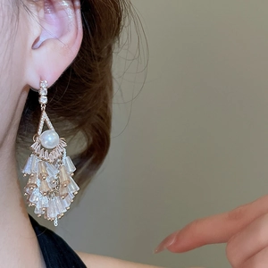 Detail von Gold-Quastenohrringen mit glitzernden Kristallen und einer weißen Rundperle