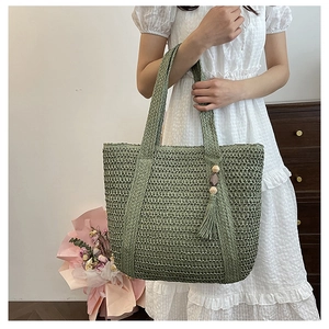 Detailed close-up of green hand-woven straw tote bag with wood bead and tassel decor