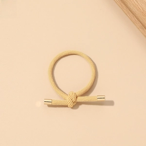 Detail of beige braided hair tie with elegant knotted design and gold metal clasps