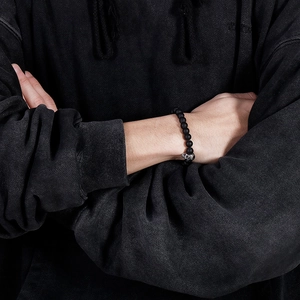 Close-up of black matte beaded bracelet with silver skull charm worn on a male wrist