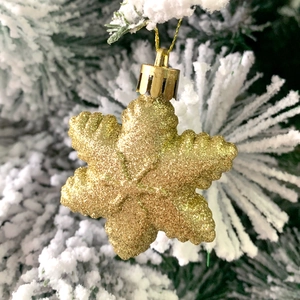 Golden glitter snowflake ornament hanging on a snowy Christmas tree branch detail