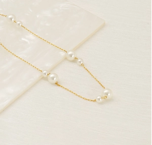 Macro detail of 18K gold stainless steel chain with alternating white pearls on marble