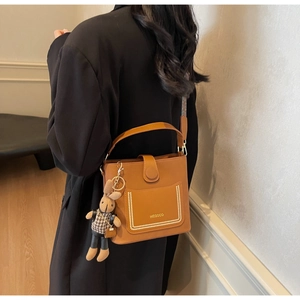 Detail of a brown leather bucket bag featuring a pearl-rimmed pocket and a cute rabbit charm