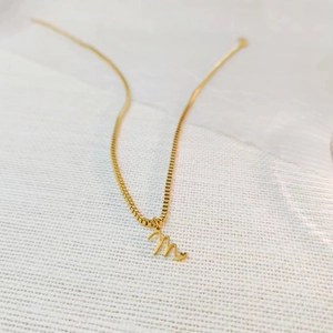 Vue macro du pendentif lettre M dorée avec détail cœur sur une chaîne à mailles