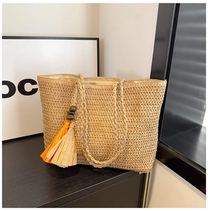 Detail of woven straw tote featuring vibrant orange and beige decorative tassels