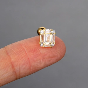 Close-up of gold stud earring with cubic zirconia rectangle held on a fingertip