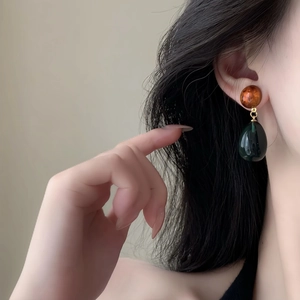 Detailed view of asymmetric water drop resin earrings worn by a model in soft light