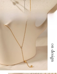 Detail of gold Y-shaped necklace with zircon pendant and metal droplet accent