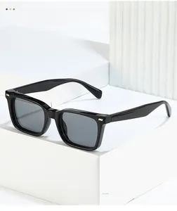 Detail showing high-gloss black square sunglasses frame with three golden metal rivets