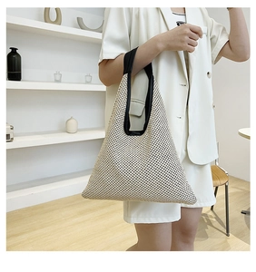 Close-up of beige woven tote bag with wide black handles and hollow mesh pattern