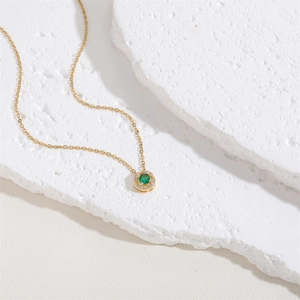 Macro shot of circular emerald pendant with zircon halo on a gold chain necklace