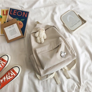 Detail of minimalist cream backpack with plush bear charm and cute rabbit badge