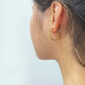 Detailed close-up of a model wearing a gold twisted hoop earring with spiral texture