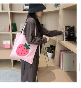 Pink canvas tote bag with strawberry embroidery worn by a model in a library