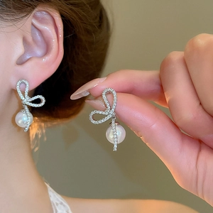 Detailed view of silver bow pearl earrings with cubic zirconia on a female model