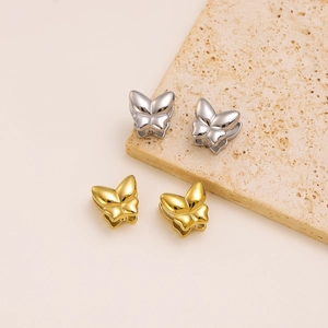 Detail of minimalist gold and silver butterfly earrings on a natural stone surface
