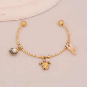 Detail view of gold cuff bracelet with blue enamel shell, sea turtle and spiral charms