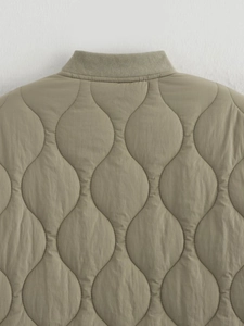 Macro detail of wave quilted texture and ribbed neckline on olive green cotton jacket