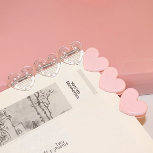 Set of heart-shaped transparent and pink plastic paper clips shown on an open book