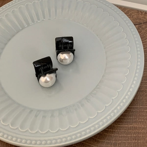 Detail of elegant black resin hair clips with white pearls on a blue rimmed ceramic plate