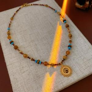 Detail of beaded sun necklace with natural brown stones and gold solar pendant
