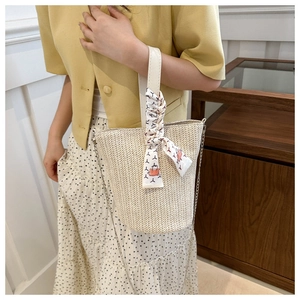 Détail d'un sac seau en paille beige avec chaîne argentée et poignée en foulard