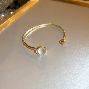 Detail of gold-plated open bangle featuring a cat-eye stone surrounded by pave diamonds
