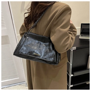 Detail of black pleated leather shoulder bag with metallic chain strap and fashion text