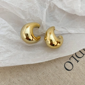 Close-up of polished gold C-shaped drop earrings on a natural fabric background
