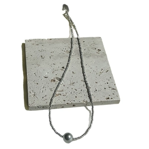 Minimalist stainless steel necklace with grey pearl pendant on stone display