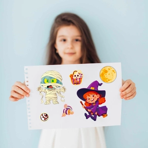 Detail of a child applying Halloween stickers including mummies and witches on paper