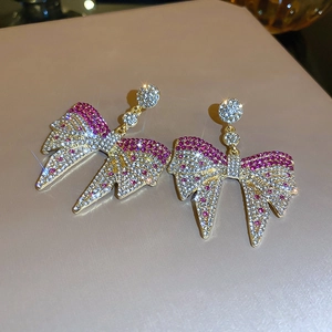 Close-up of golden bow earrings with pink and white rhinestones on beige background