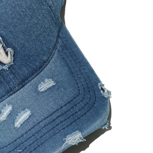 Close-up of distressed blue denim baseball cap showing ripped details and stitching
