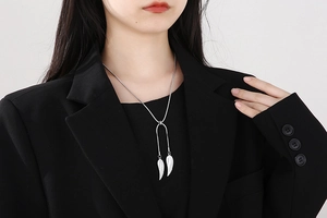 Detail shot of silver angel wing pendant necklace on model with black suit blazer