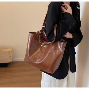 Detail of dark brown oil wax leather tote bag with elegant gold metal bar accent