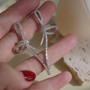 Macro shot of silver bow earrings with sparkling zircons held to show size scale