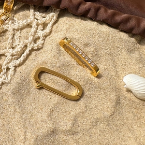 Detailed view of gold oval earrings with white zircons on beach sand and sea shell
