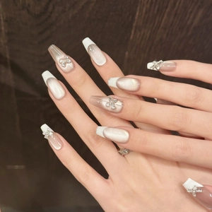 Detail of champagne cat-eye press-on nails with 3D silver bows and white French tips
