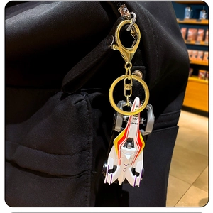 White mini racing car keychain accessory hanging on a black backpack with gold buckle