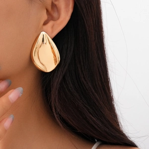 Detailed view of large golden drop-shaped earrings with a high-polished metallic finish
