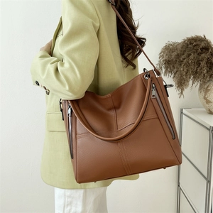 Brown litchi grain leather tote bag with side metal zippers worn by model in a green suit