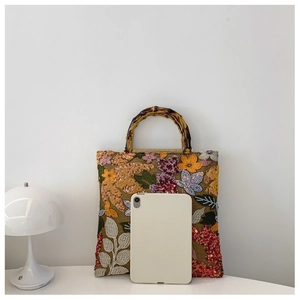 Linen handbag with floral embroidery and bamboo handle next to a tablet for size reference