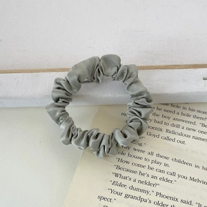 Close-up of sage green satin scrunchie with silky luster on vintage book pages