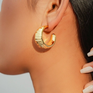 Close-up of a woman wearing chunky gold C-shaped hoop earrings with hammered texture