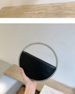 Detail of elegant black semi-circular evening clutch featuring a large rhinestone handle