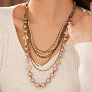 Detail of multi-layer pearl necklace featuring diamond clover charms on a knitted sweater